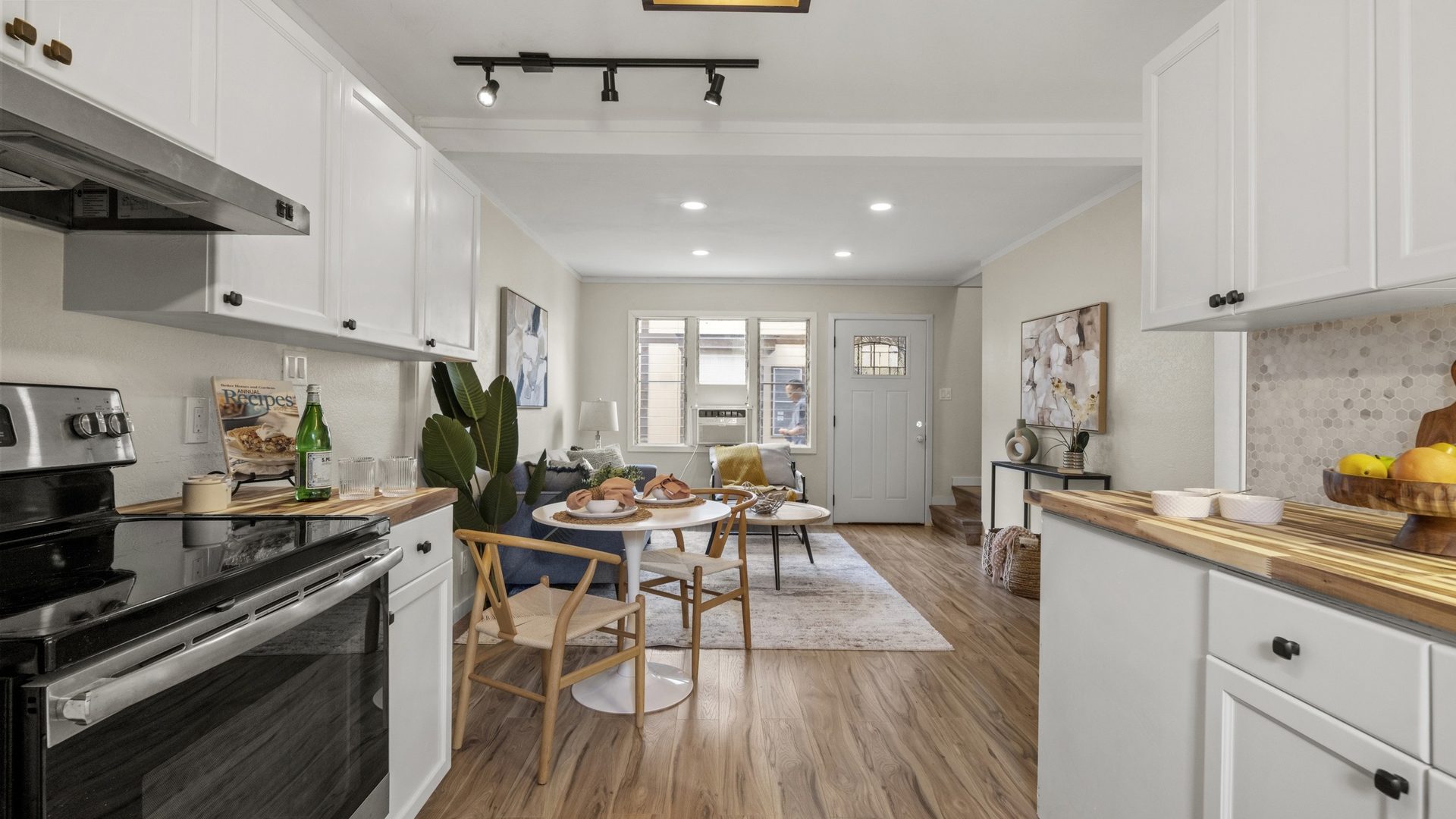 Kitchen with white cabinets, butcher-block counters and a stainless range, opening to a dining area with a round table and wood chairs under track lights